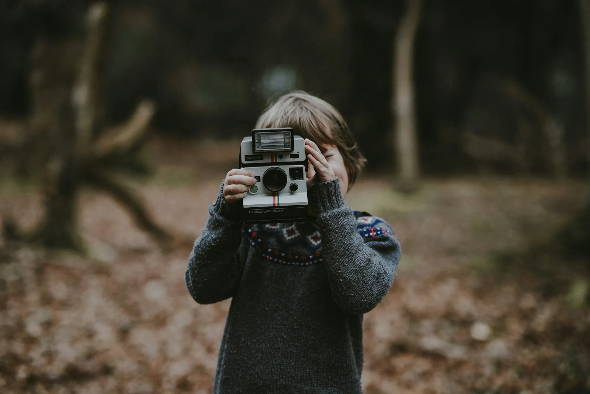A child holding an instant camera up to the eye in an autumn forest